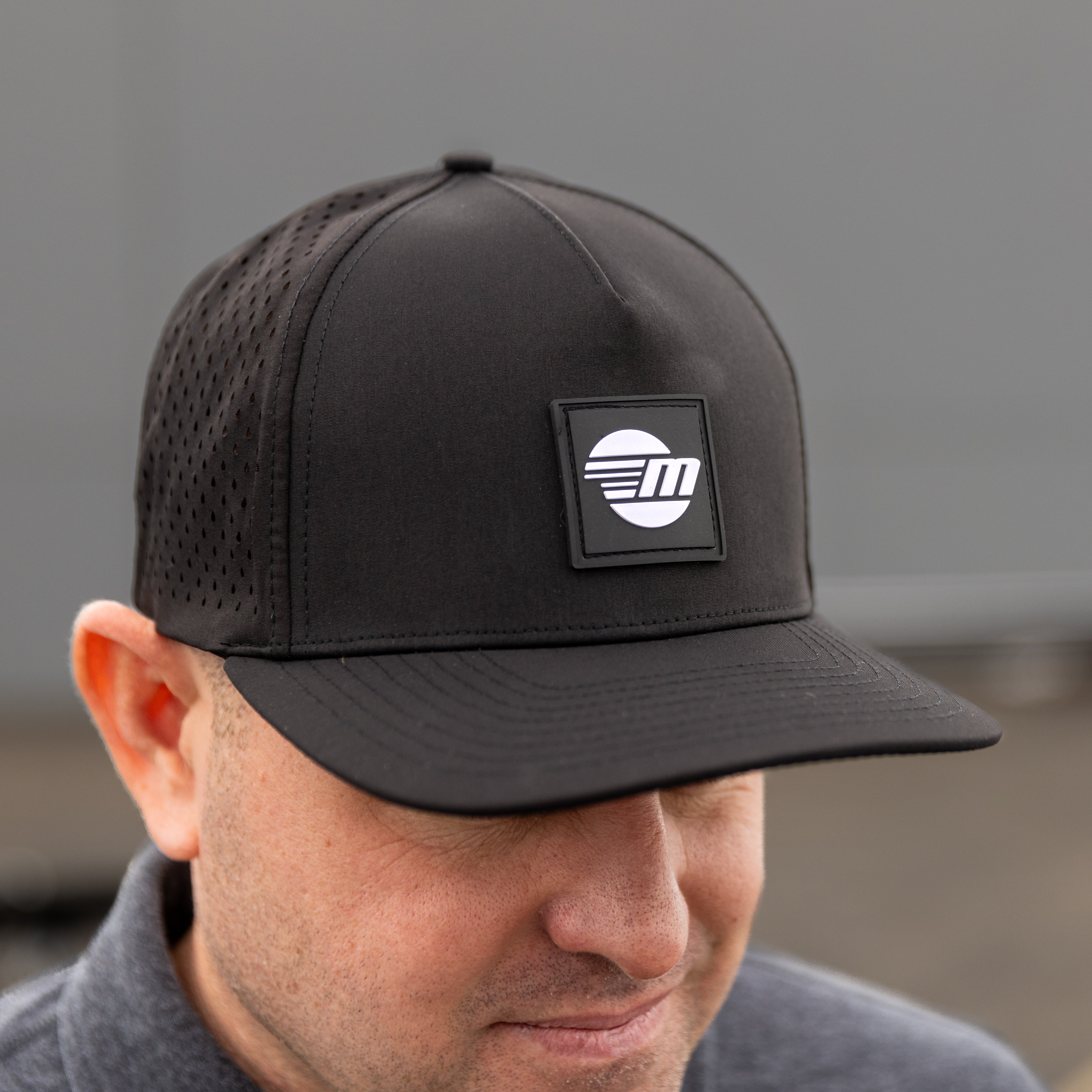 Black Malibu Swell hat with a perforated crown and a square logo patch on the front, worn by a person with short hair.