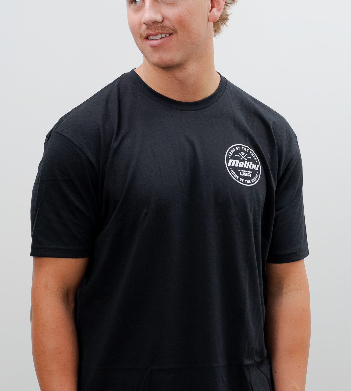 Black Malibu Brave T-shirt with a small white circular logo on the chest reading "Land of the Free, Made in the USA, Home of the Brave.