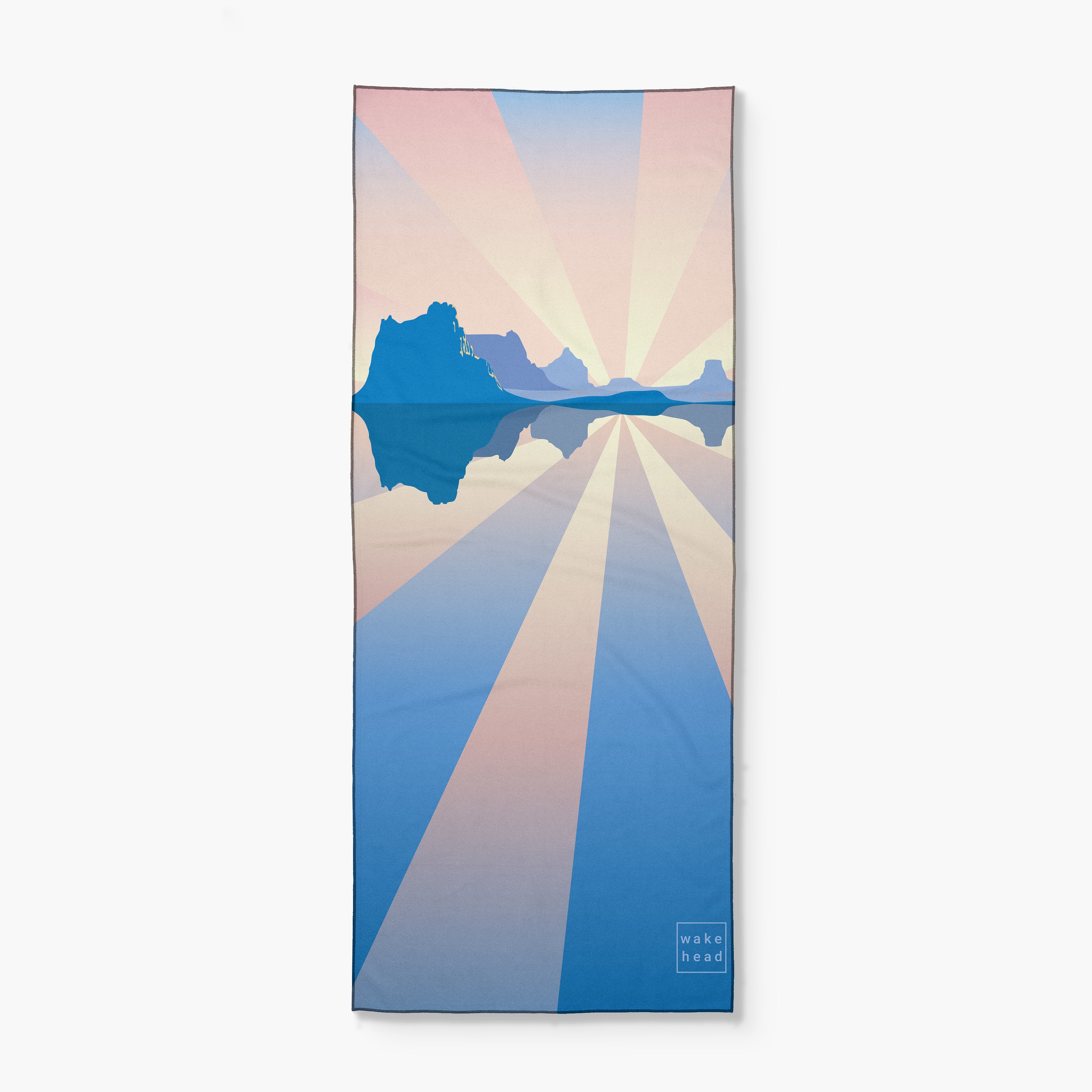 A colorful towel featuring a stylized sunset over mountains and water, with radiating pastel sun rays and the "Wake Head" logo in the corner.