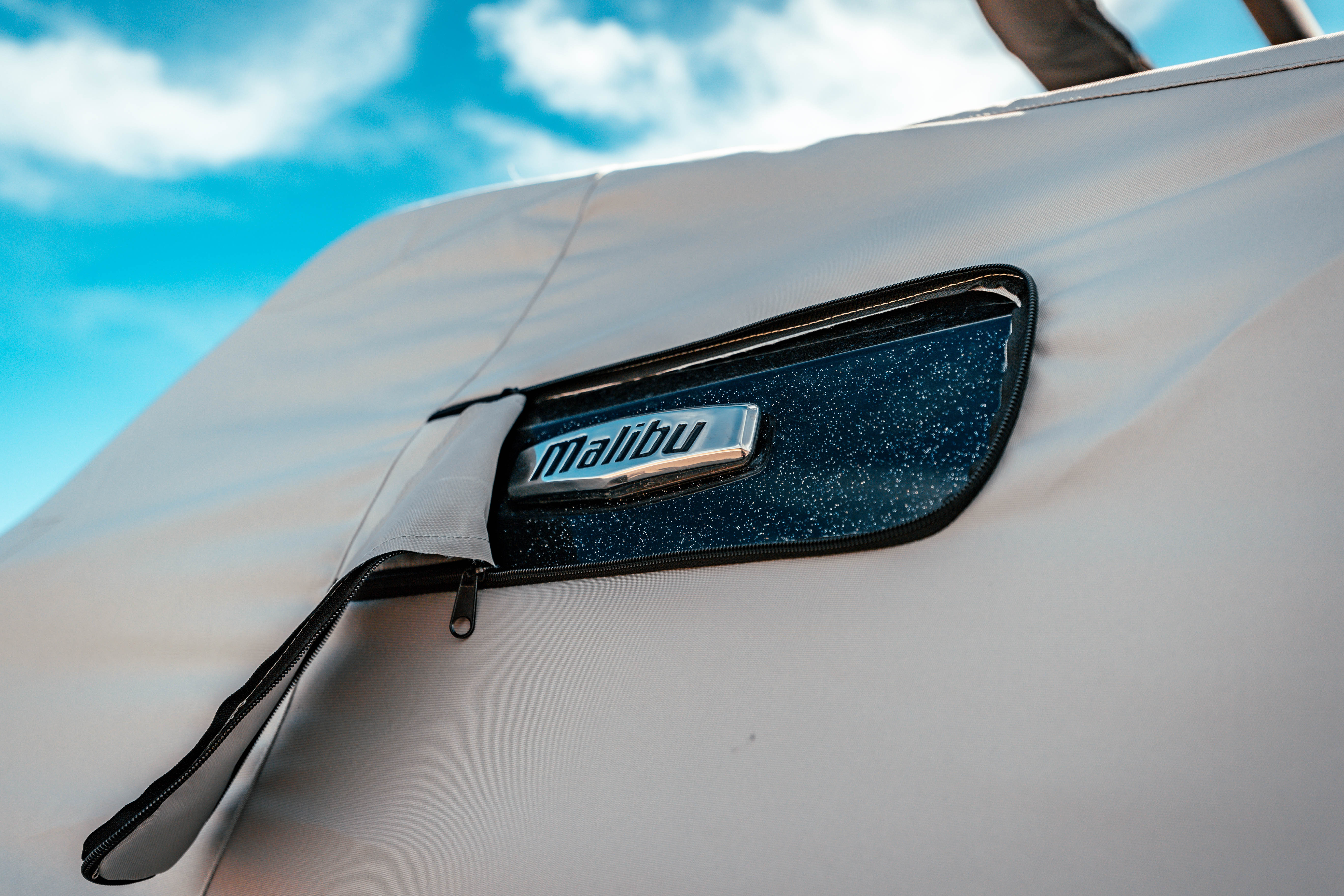 Close-up of a Malibu boat cover with a zippered pocket featuring a "Malibu" logo, designed for 23 LSV with bow cleats and G3 tower.